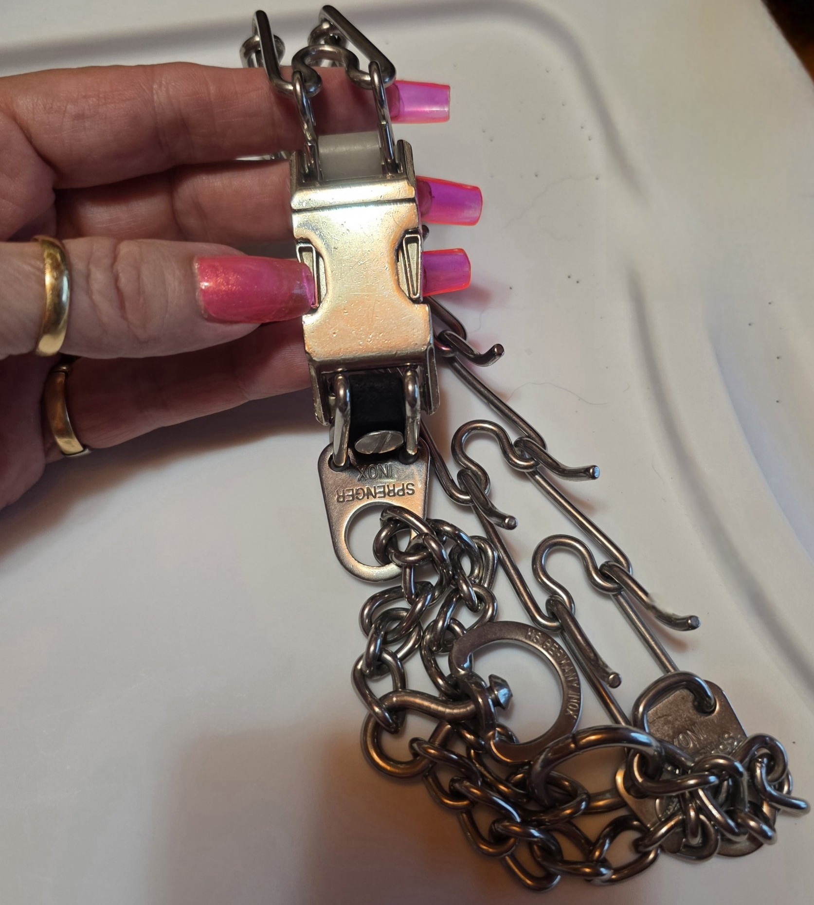 A hand with long pink nails holding the quick-release buckle on a Herm Sprenger prong collar